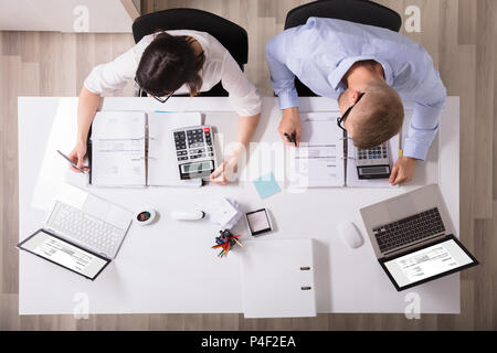 Two Young Businesspeople Calculating Invoice With Calculator Stock Photo