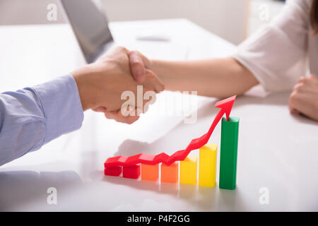 Close-up Of Increasing Multi Colored Graph With Red Arrow In Front Of Businesspeople Shaking Hands Stock Photo