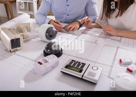 Various Security Equipments In Front Of Two Architects Planning Project On Blueprint Stock Photo