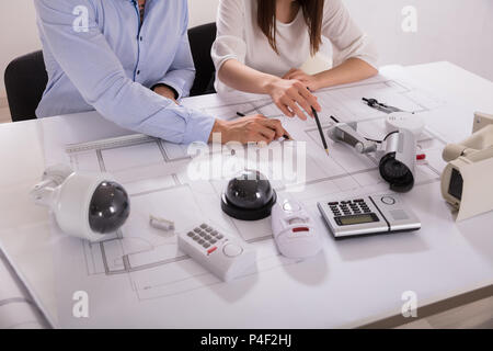 Various Security Equipments In Front Of Two Architects Planning Project On Blueprint Stock Photo