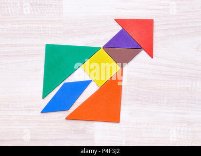Flay lay of colorful tangram figures arranged in shape of rocket on wooden table. Stock Photo