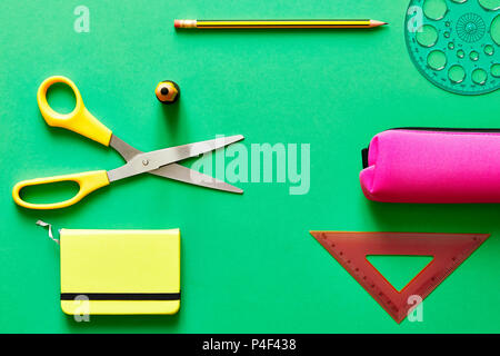 School tools such as yellow scissors, pencil, ruler, eraser, and pencil case, over a blue flatlay in blue from above Stock Photo