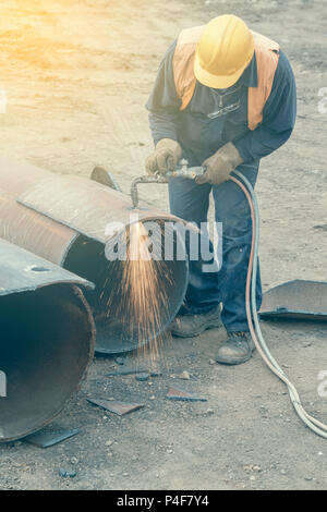 Welder worker with cutting torch, cutting hole in a steel pipe. Oxygen-propane cutting torch, used to cut a steel pipe. Vintage style. Stock Photo