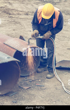 Welder worker with cutting torch, cutting hole in a steel pipe. Oxygen-propane cutting torch, used to cut a steel pipe. Vintage style. Stock Photo