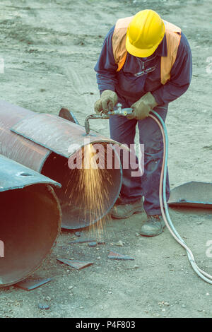 Welder worker with cutting torch, cutting hole in a steel pipe. Oxygen-propane cutting torch, used to cut a steel pipe. Vintage style. Stock Photo