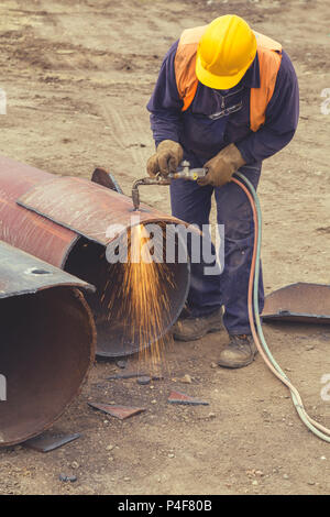 Welder worker with cutting torch, cutting hole in a steel pipe. Oxygen-propane cutting torch, used to cut a steel pipe. Vintage style. Stock Photo