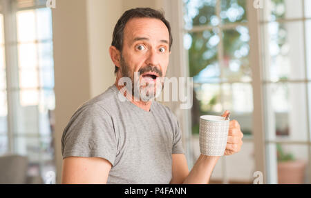 Middle age man drinking coffee in a cup scared in shock with a surprise face, afraid and excited with fear expression Stock Photo