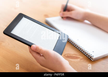 Girl is reading ebook on digital tablet device and is taking notes Stock Photo