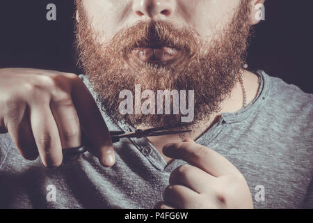 man cuts his beard with scissors, photo close-up on a black background, toned image Stock Photo