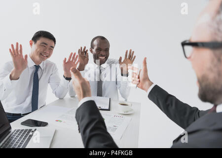 multicultural cheerful businessmen sitting at workplace with documents and laptop Stock Photo