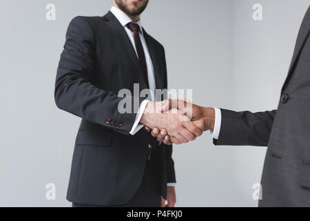 partial view of multicultural businessmen shaking hands after meeting isolated on grey Stock Photo