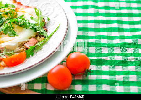Fried eggs with arugula and tomatoes cherry on white plate and checkered cloth. Copy space Stock Photo