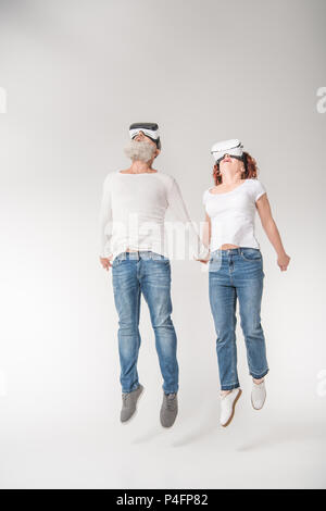 senior couple jumping while using virtual reality headsets, isolated on white Stock Photo