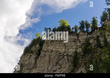 view from below upwards on steep rocky woody limestone cliffs against the sky Stock Photo