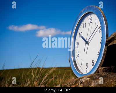 Photo of a chrome clock outdoors sitting on rural stone on the morning of a bright sunny day. Stock Photo