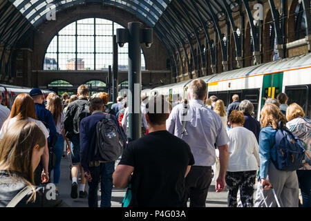 Commuters walk along a platform towards the exit with trains alongside them in Kings Cross railway station, London, UK Stock Photo