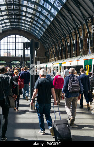 Commuters walk along a platform towards the exit with trains alongside them in Kings Cross railway station, London, UK Stock Photo