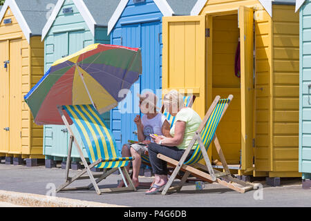 Bournemouth, Dorset, UK. 22nd June 2018. UK weather: lovely warm sunny day at Bournemouth beaches as visitors head to the seaside to make the most of the sunshine, as the forecast is for temperatures to increase further. Two women in deckchairs under parasol on promenade in front of beach huts. Credit: Carolyn Jenkins/Alamy Live News Stock Photo