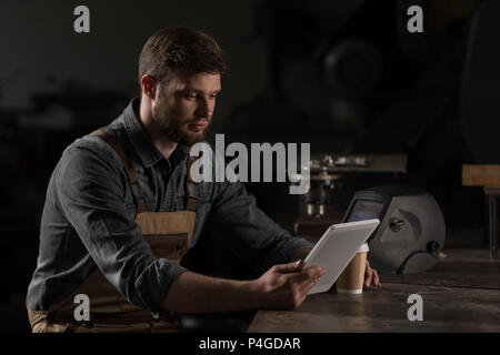 young male workman with paper cup of coffee using digital tablet Stock Photo