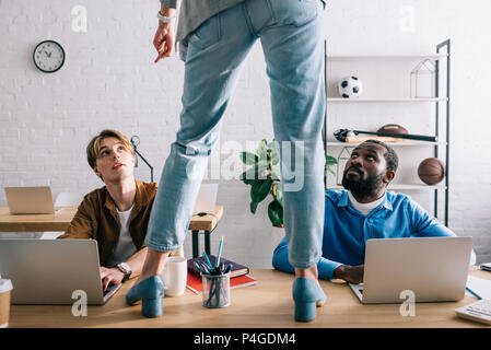 cropped image of female standing on table and pointing by finger to two multicultural businessmen working on laptops Stock Photo