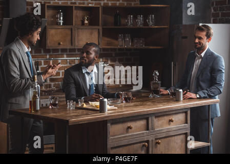 three multiethnic male friends in suits talking while drinking alcohol together Stock Photo