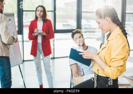 Businesswoman holding notebook by her colleagues in light workspace Stock Photo