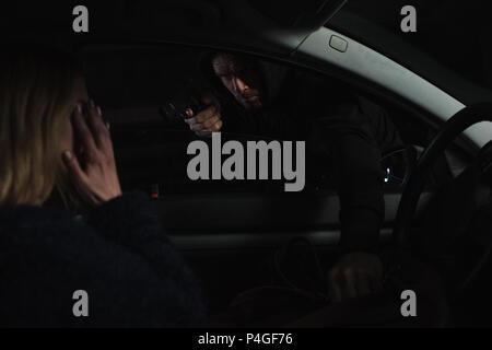 male thief aiming by gun and stealing bag from woman sitting in car Stock Photo