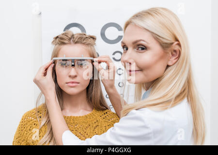 female patient and optician with trial frame and eye chart behind