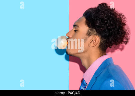 Close up of handsome man blowing gum on pink and blue background Stock Photo