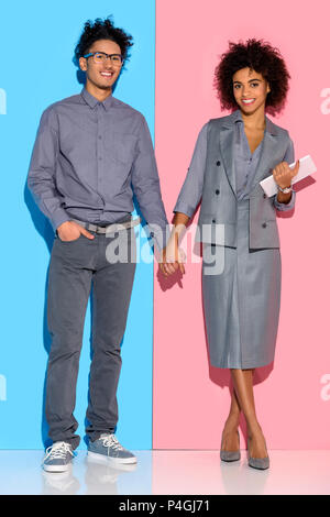 Young african amercian girl holding tablet and hand of stylish guy on pink and blue background Stock Photo