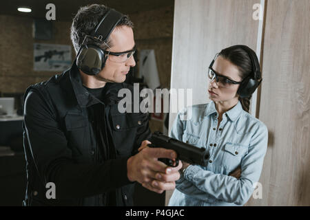 male instructor describing gun to female client in shooting gallery Stock Photo