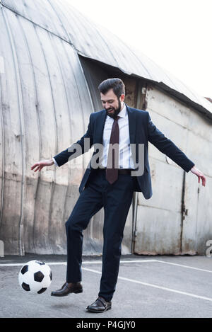 smiling businessman in suit playing soccer on street Stock Photo