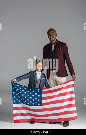 african american family looking at camera while boy holding american flag in hands on grey background Stock Photo