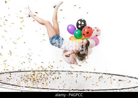 smiling girl holding colorful balloons and falling on trampoline isolated on white Stock Photo