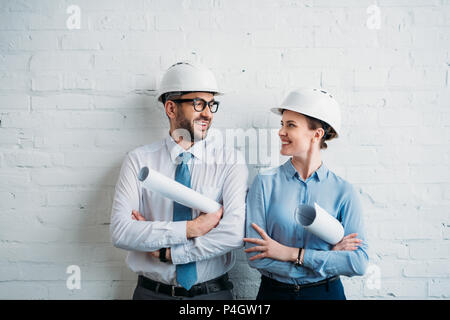 architects in hard hats standing in front of white brick wall with blueprints Stock Photo