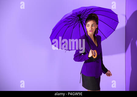 stylish african american girl posing with purple umbrella at ultra violet wall Stock Photo