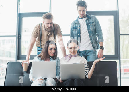 Successful business people working on laptops while sitting on sofa in modern light office Stock Photo