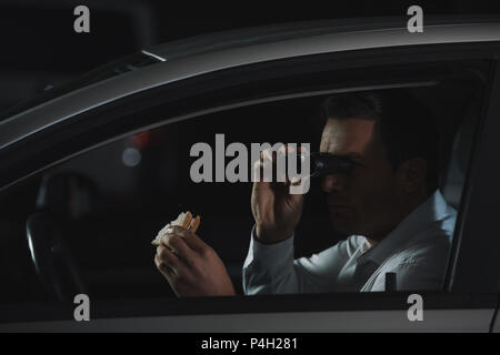 undercover male agent doing surveillance by binoculars and drinking coffee  in car Stock Photo - Alamy