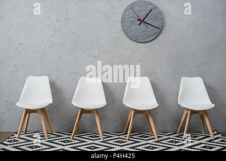 Row of empty white chairs in a waiting room at company with wall clock Stock Photo