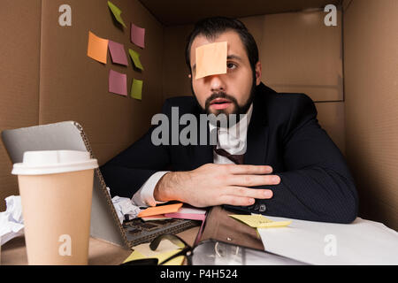 exhausted businessman with sticky note on forehead in box Stock Photo