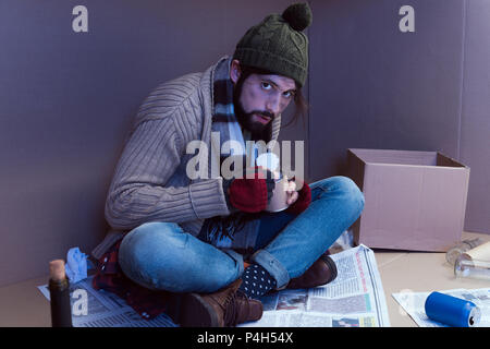 homeless man eating canned food in cardboard box Stock Photo