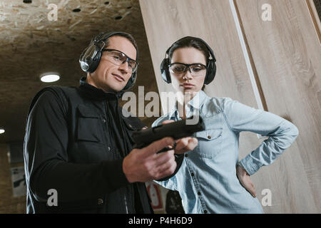 male instructor describing pistol to female client in shooting gallery Stock Photo