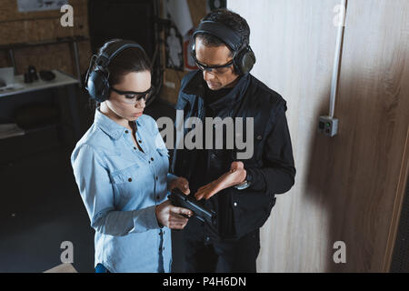 male instructor describing gun to female customer in shooting range Stock Photo