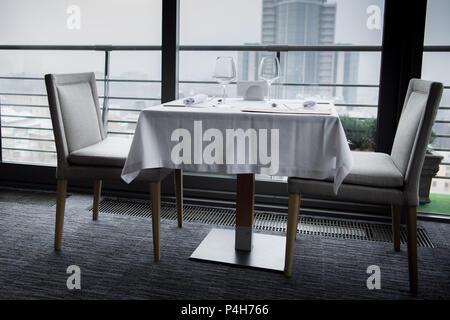 table with arranged cutlery, empty wineglasses and menu on white tablecloth in restaurant