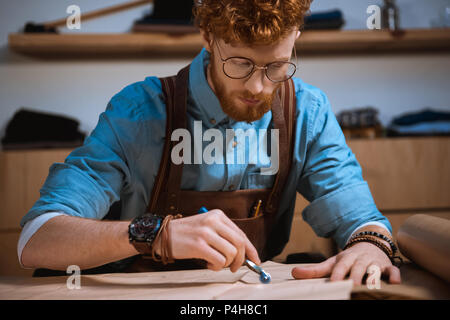focused young male fashion designer in eyeglasses making sewing patterns at workplace Stock Photo