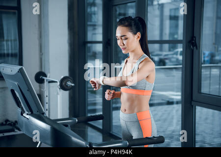 young athletic sportswoman checking fitness tracker while running on treadmill at gym Stock Photo