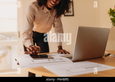 Businesswoman using a tablet pc while working on laptop computer at home. Woman entrepreneur standing beside the table using tablet pc while working o Stock Photo