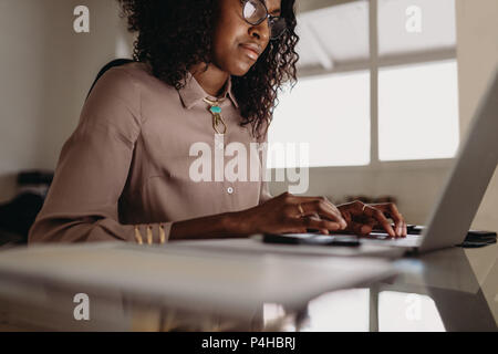 Businesswoman working on laptop computer from home. Woman entrepreneur sitting at home working on laptop with business documents on the table. Stock Photo