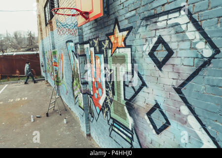 man painting colorful graffiti on wall with basketball hoop Stock Photo