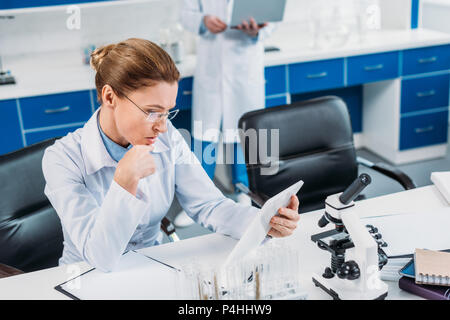 selective focus of female scientist using tablet at workplace with colleague behind in lab Stock Photo
